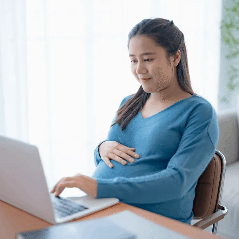Pregnant woman in a blue sweater working on a laptop