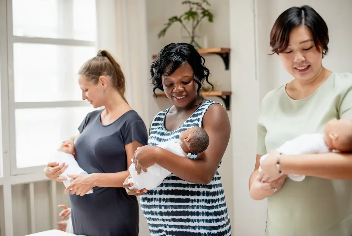 Three mothers standing together, each holding a newborn baby