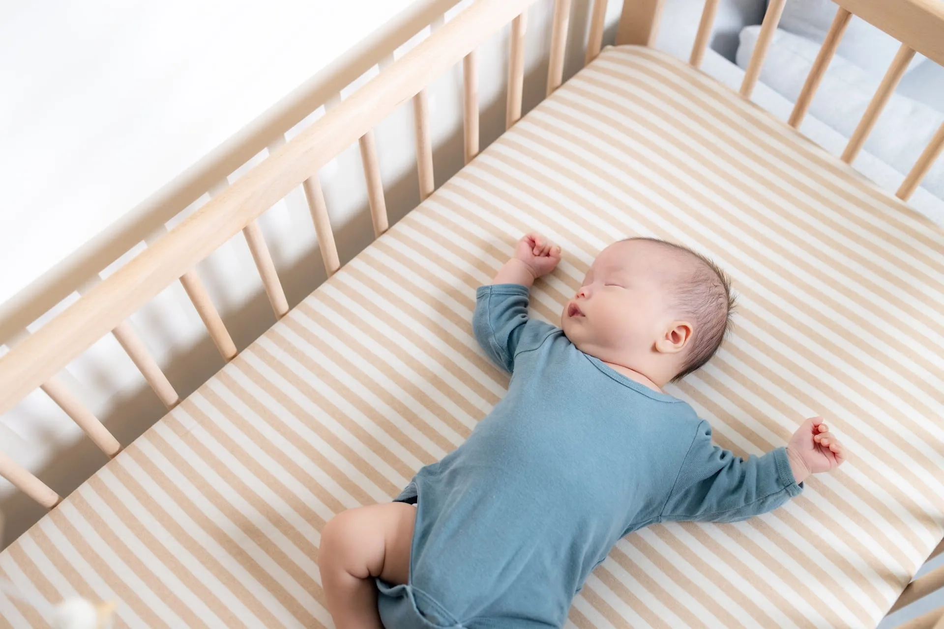 Baby in a blue bodysuit sleeping on its back in a crib with a striped sheet
