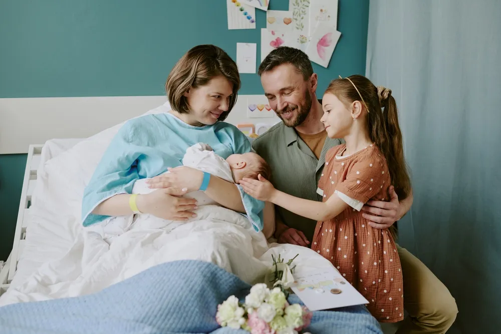 Mother in a hospital bed holding her newborn as the father and their young daughter lean in close