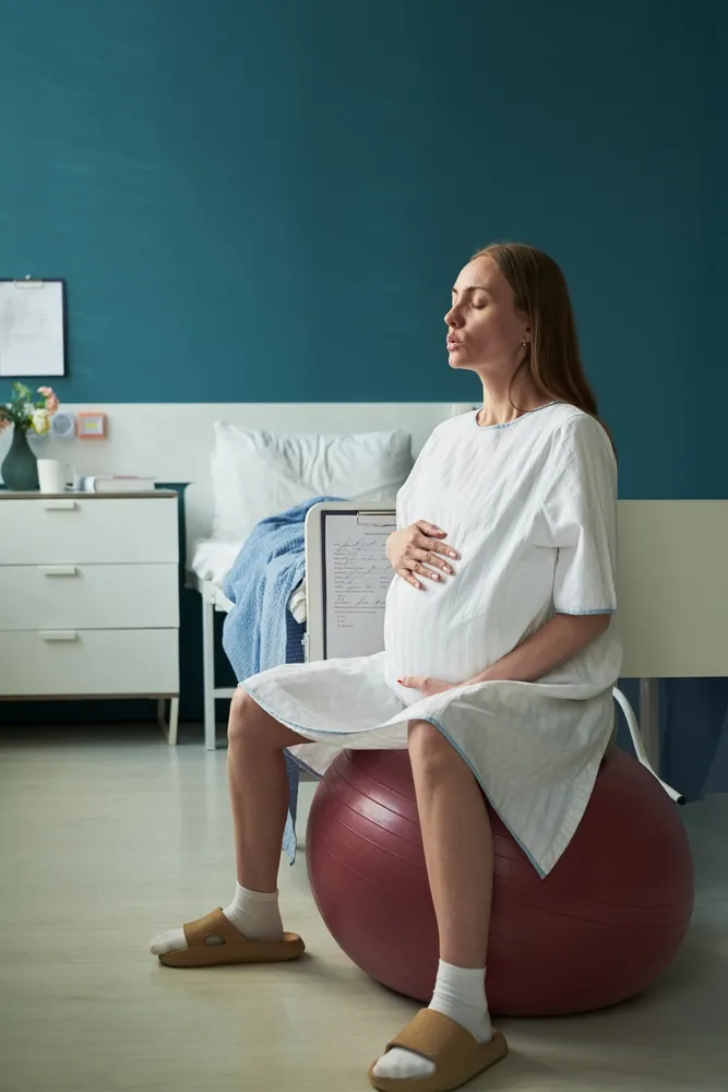 Pregnant woman in a hospital gown sitting on a birth ball with her eyes closed