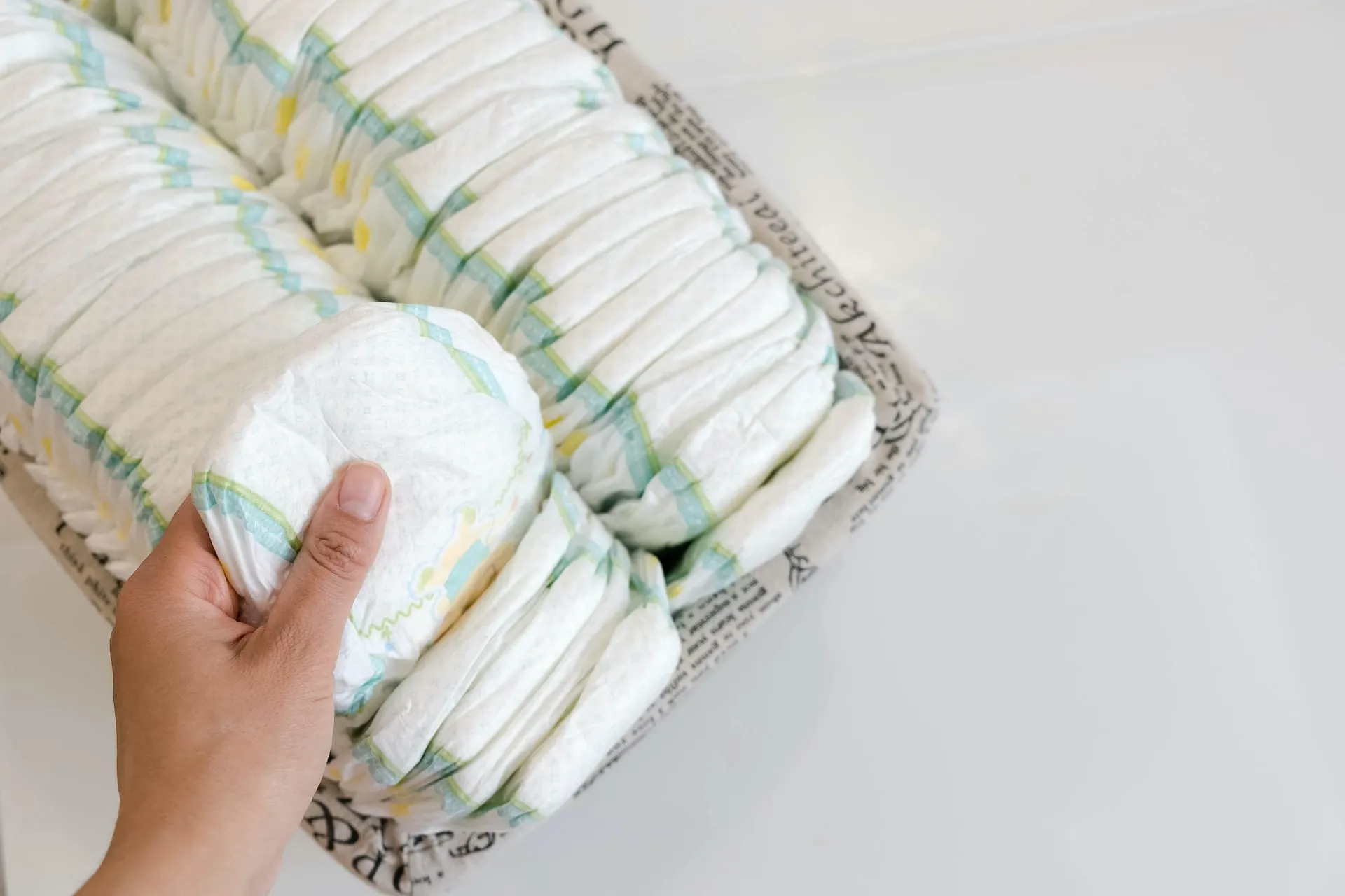 Hand taking a clean diaper from a basket full of folded diapers